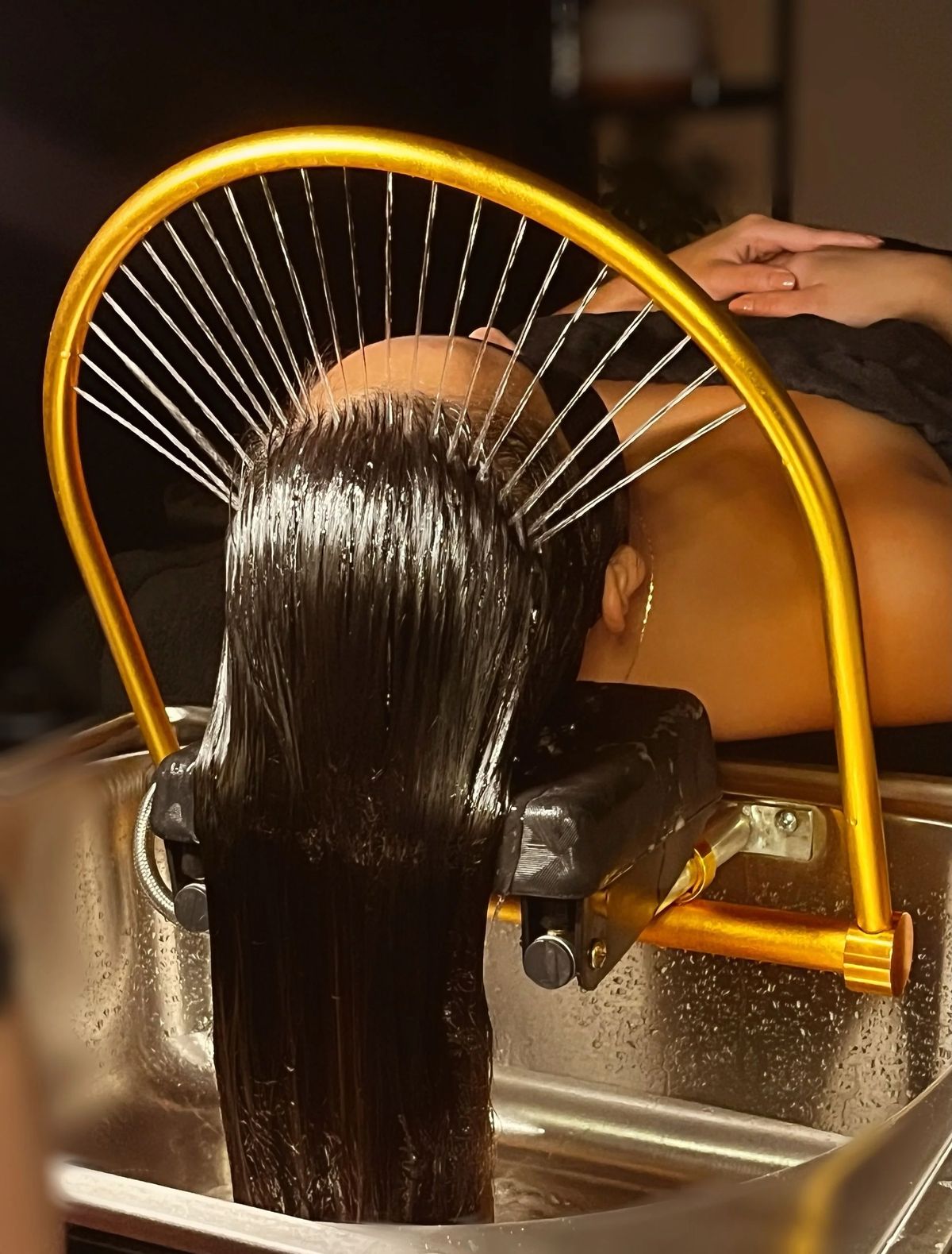 Hair being rinsed beneath a head spa water arch